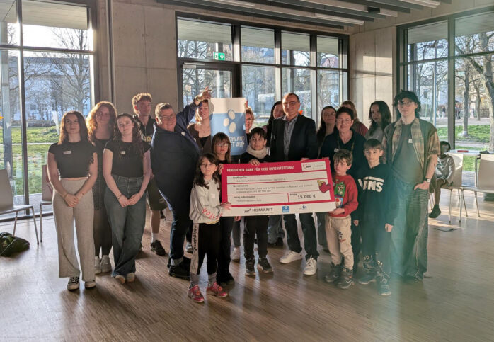 Freude über die Unterstützung für „Balu und Du“: Vertreterinnen und Vertreter der AWO Saarland, der htw saar sowie Studierende und teilnehmende Kinder präsentieren den symbolischen Spendenscheck über 15.000 Euro von Homanit und der Organisation Deutschland rundet auf zur Förderung des Mentoring-Projekts.