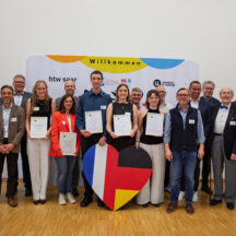 Gruppenfoto der Verleihung des Helmut Schmidt – Valéry Giscard d’Estaing-Preises 2026 am Deutsch-Französischen Hochschulinstitut (DFHI): Die ausgezeichneten Studierenden stehen gemeinsam mit Vertreterinnen und Vertretern des DFHI-Fördervereins, der htw saar und der Université de Lorraine vor einer Veranstaltungswand mit den Logos der Hochschulen. Einige der Preisträgerinnen und Preisträger halten ihre Urkunden in den Händen. Im Vordergrund steht ein großes Herz in den Farben der deutsch-französischen Flaggen.